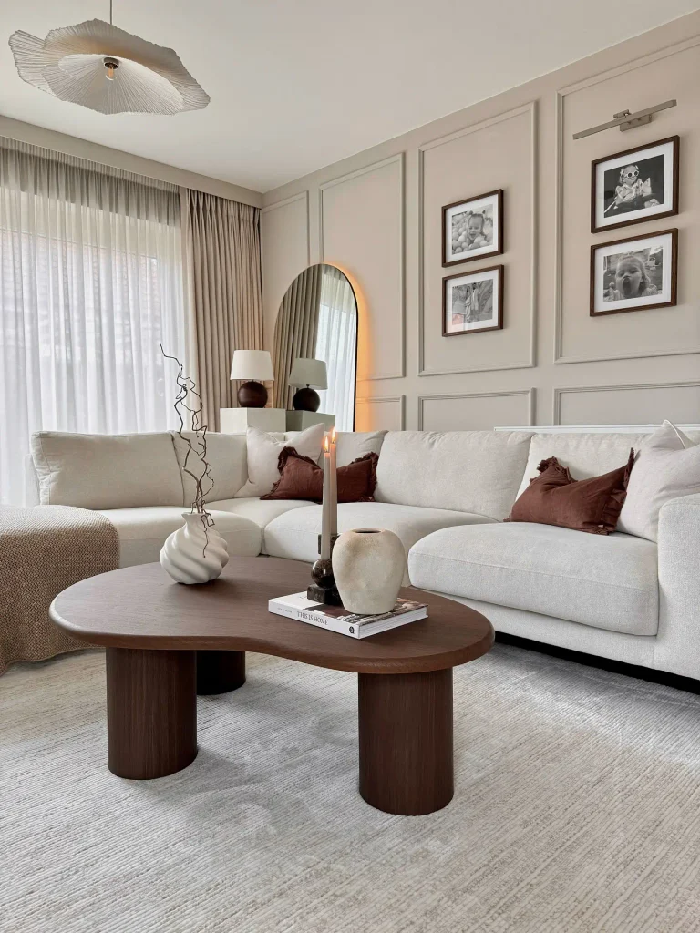 Living room inspo ideas with a cream sectional, beige wall paneling, black framed photos, and a kidney shaped walnut coffee table