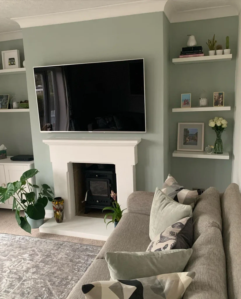 Sage green living room with a white fireplace surround, floating alcove shelves, and a gray sofa with mint cushions