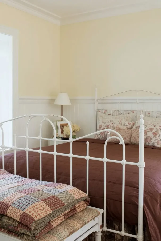 White iron bed with a chocolate floral print duvet and a patchwork quilt in a cream cottage bedroom