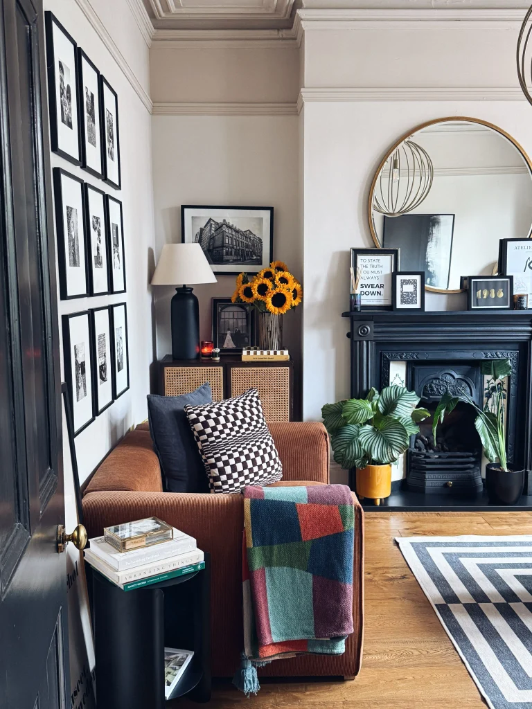 Black and white photo gallery wall beside a rust leather armchair with a checkered cushion and patchwork throw