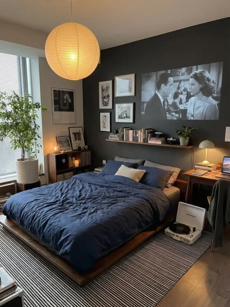 Bedroom with navy bedding, a charcoal accent wall, black-and-white framed prints, a book ledge and a large paper lantern pendant
