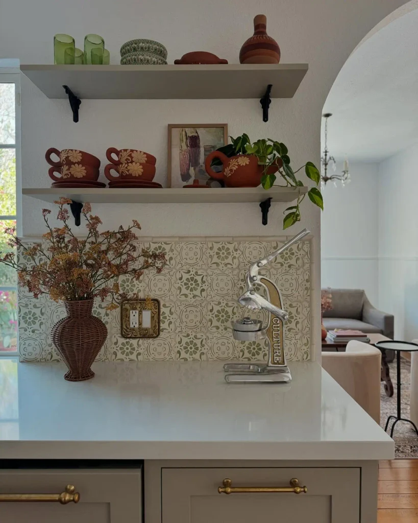Open shelves on black iron brackets with flower painted terracotta cups, green glass tumblers, and a pothos