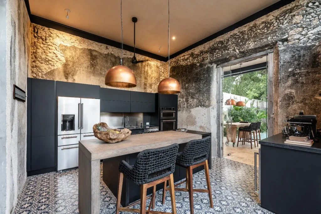 Raw stone kitchen walls with matte black cabinets, copper dome pendants, and blue and cream cement floor tiles