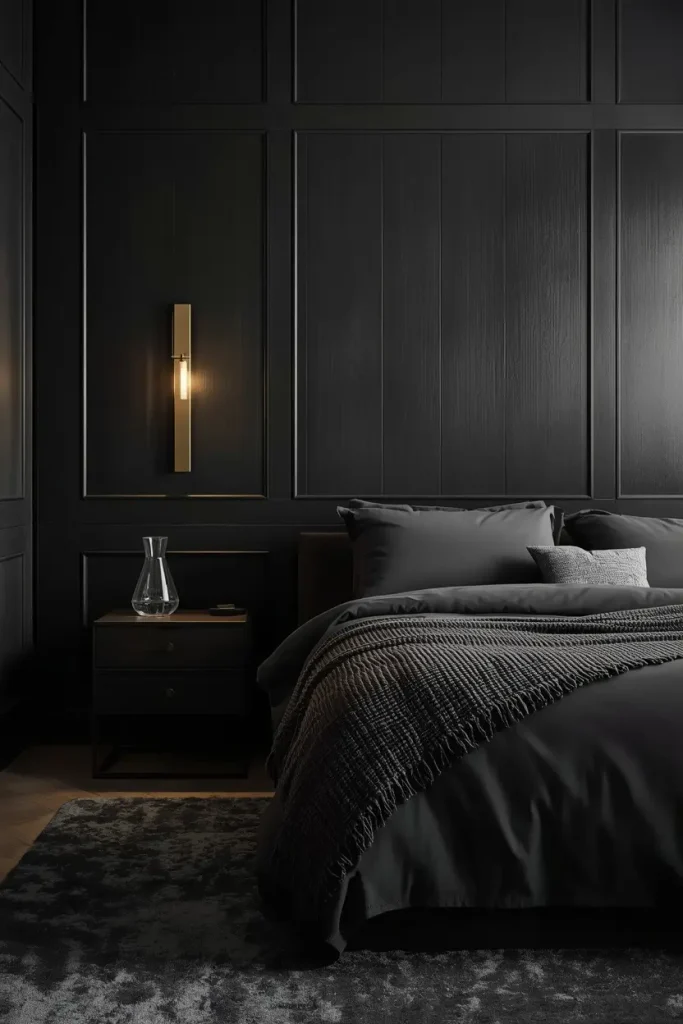 Floor-to-ceiling black panel headboard wall with brass sconces and charcoal bedding in a hotel-style suite