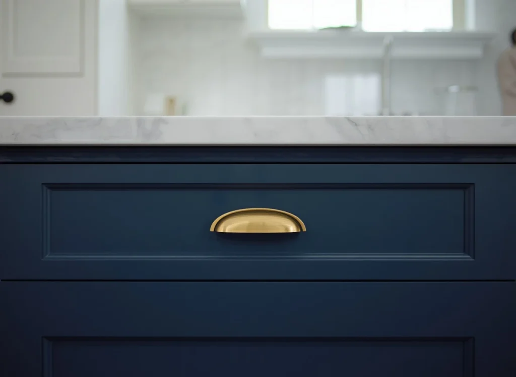 Two-tone kitchen cabinets close up with a navy blue drawer, a brass cup pull, and a white marble countertop