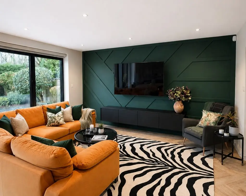 Deep emerald geometric accent wall with a black media unit, an orange velvet sectional, and a zebra print rug