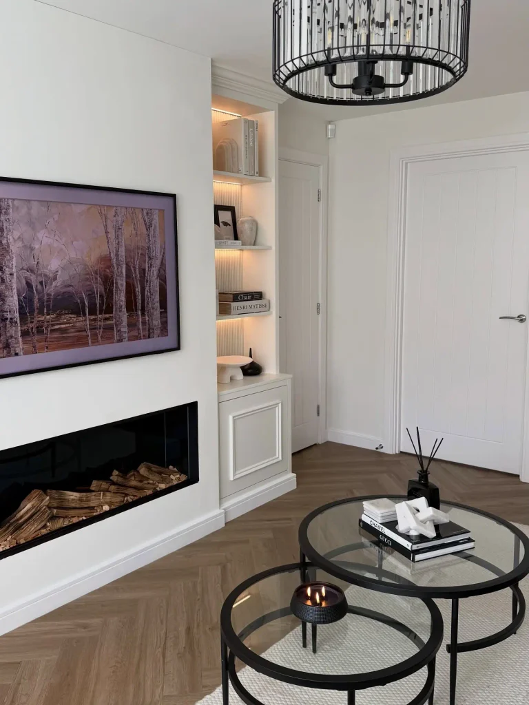 Built in alcove shelves with warm LED lights beside a linear fireplace under a TV showing birch tree art
